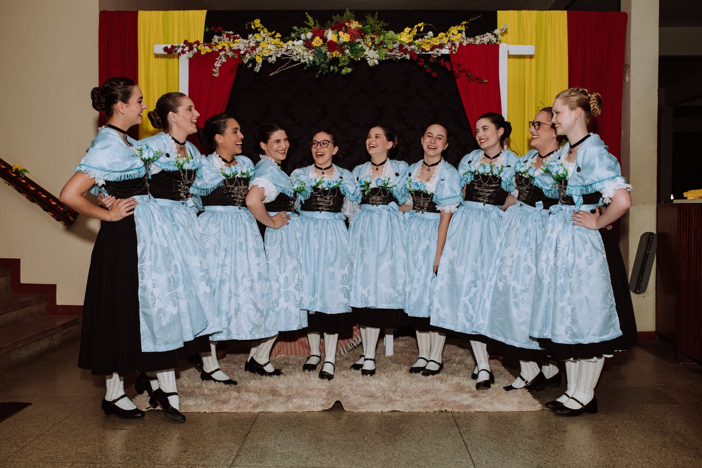 Dançarinas do Tanzgruppe Rothenburg reunidas em traje azul-claro, sorrindo umas para as outras